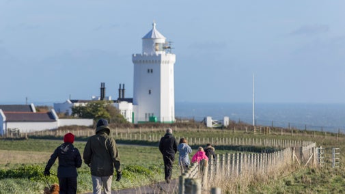 A group of people in winter clothes walking towards a white-painted lighthouse
